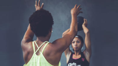 Two women passing a kettleball overhead
